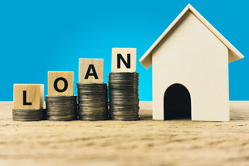 Tiles spelling the word load next to a small model of a home loan.