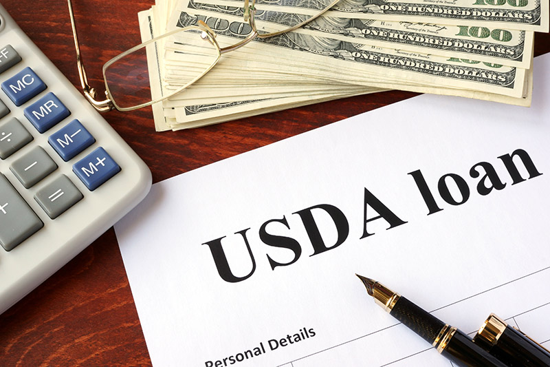 A calculator & stack of money sits on a USDA loan application.