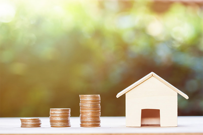 A small wooden model of a home next to stacks of quarters representing home loans.